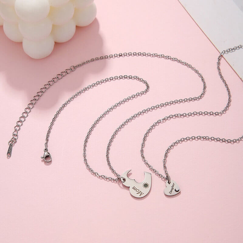 Matching mother and daughter heart necklace set with sun and moon cutout pendants on a cream silk background.