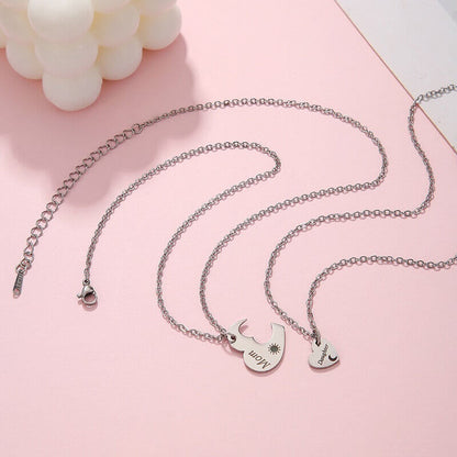 Matching mother and daughter heart necklace set with sun and moon cutout pendants on a cream silk background.